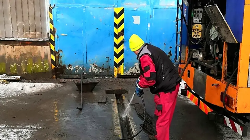 Pracovník s vysokotlakou pistolí čistí odtokový žlab u tlakového vozu